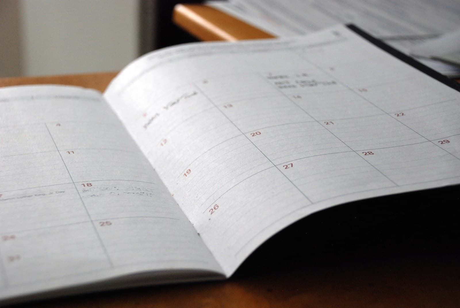 An open paper monthly planner lying on a wooden desk with a few handwritten appointments in its date boxes