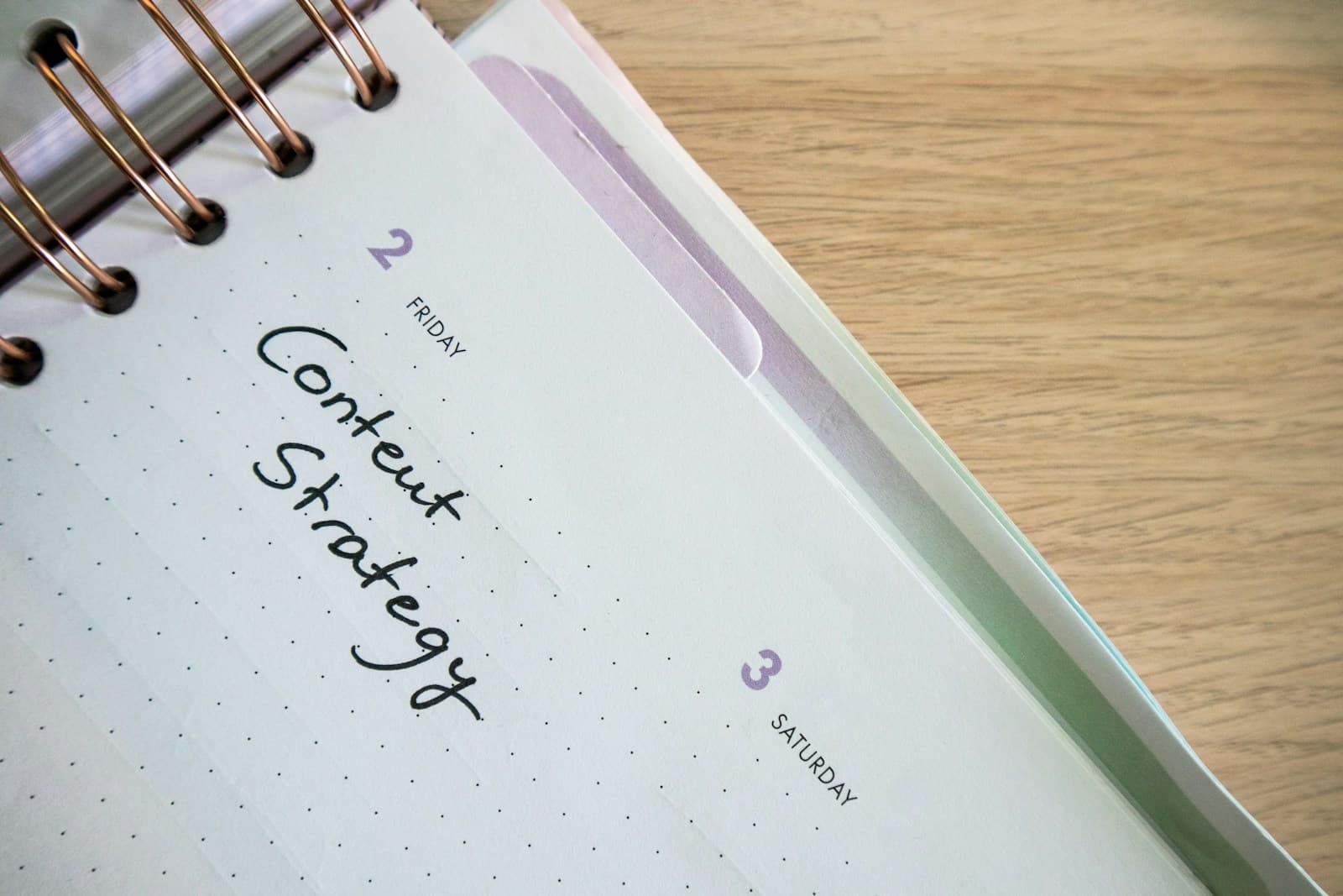 A spiral planner open on a wooden desk with the words Content Strategy handwritten on Friday's page