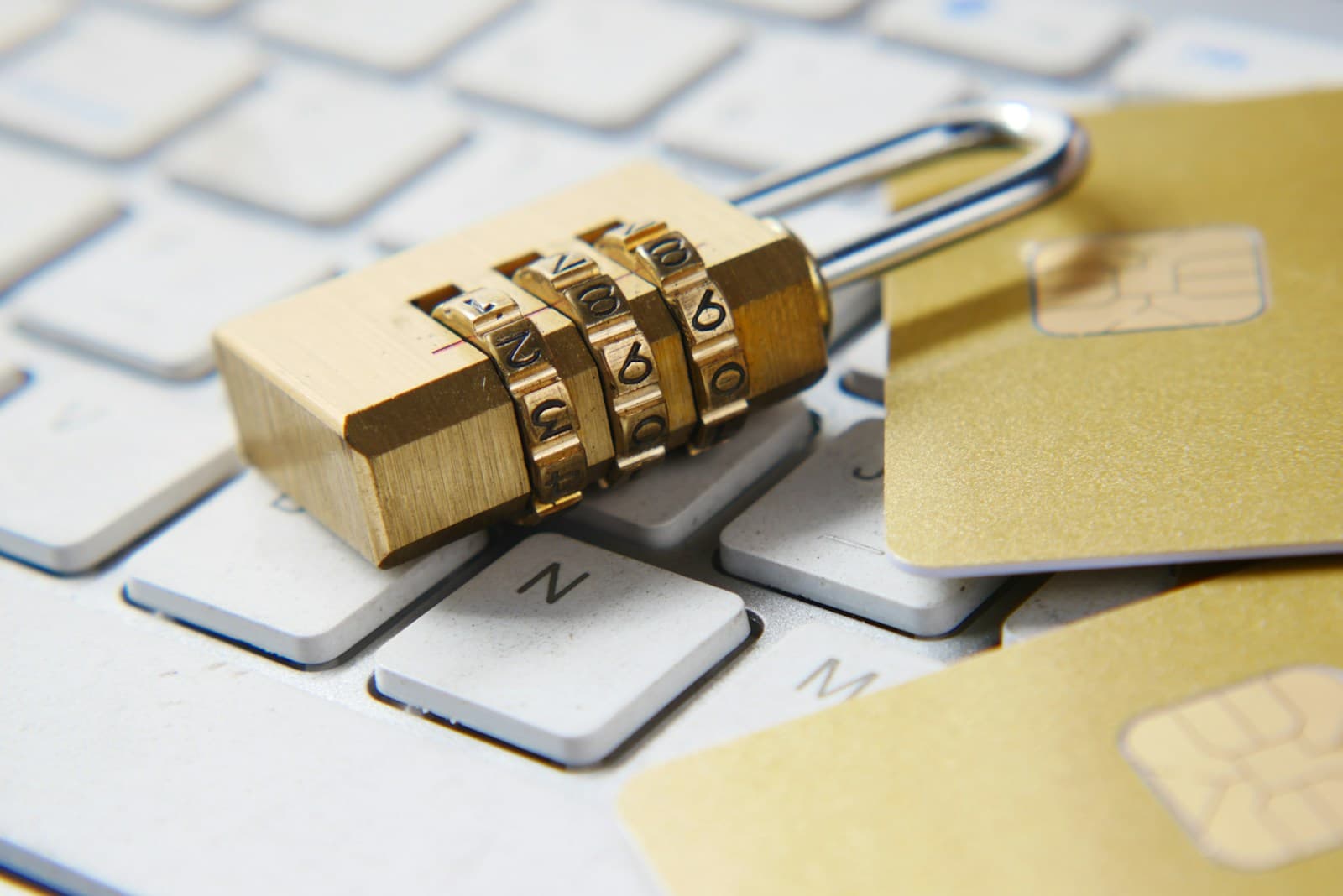 Brass combination padlock and gold payment cards resting on a white computer keyboard