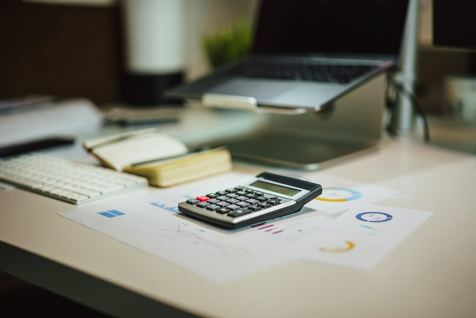 A desk calculator lying on printed charts and reports next to a laptop and keyboard