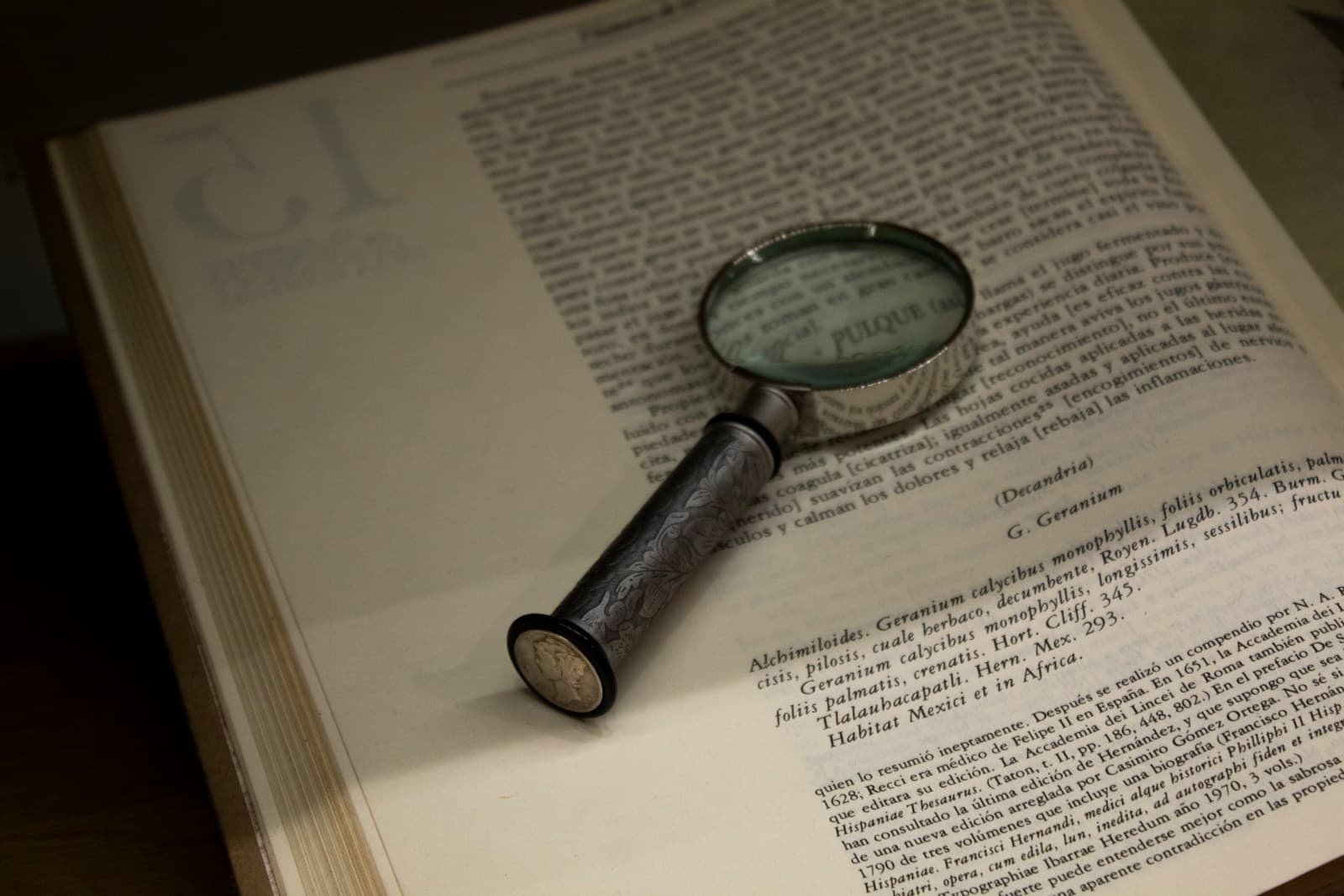 A silver magnifying glass resting on the open page of an old printed book, enlarging the text beneath it