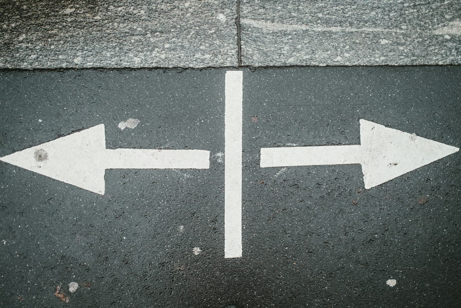 Two white arrows painted on dark asphalt pointing in opposite directions, separated by a white line