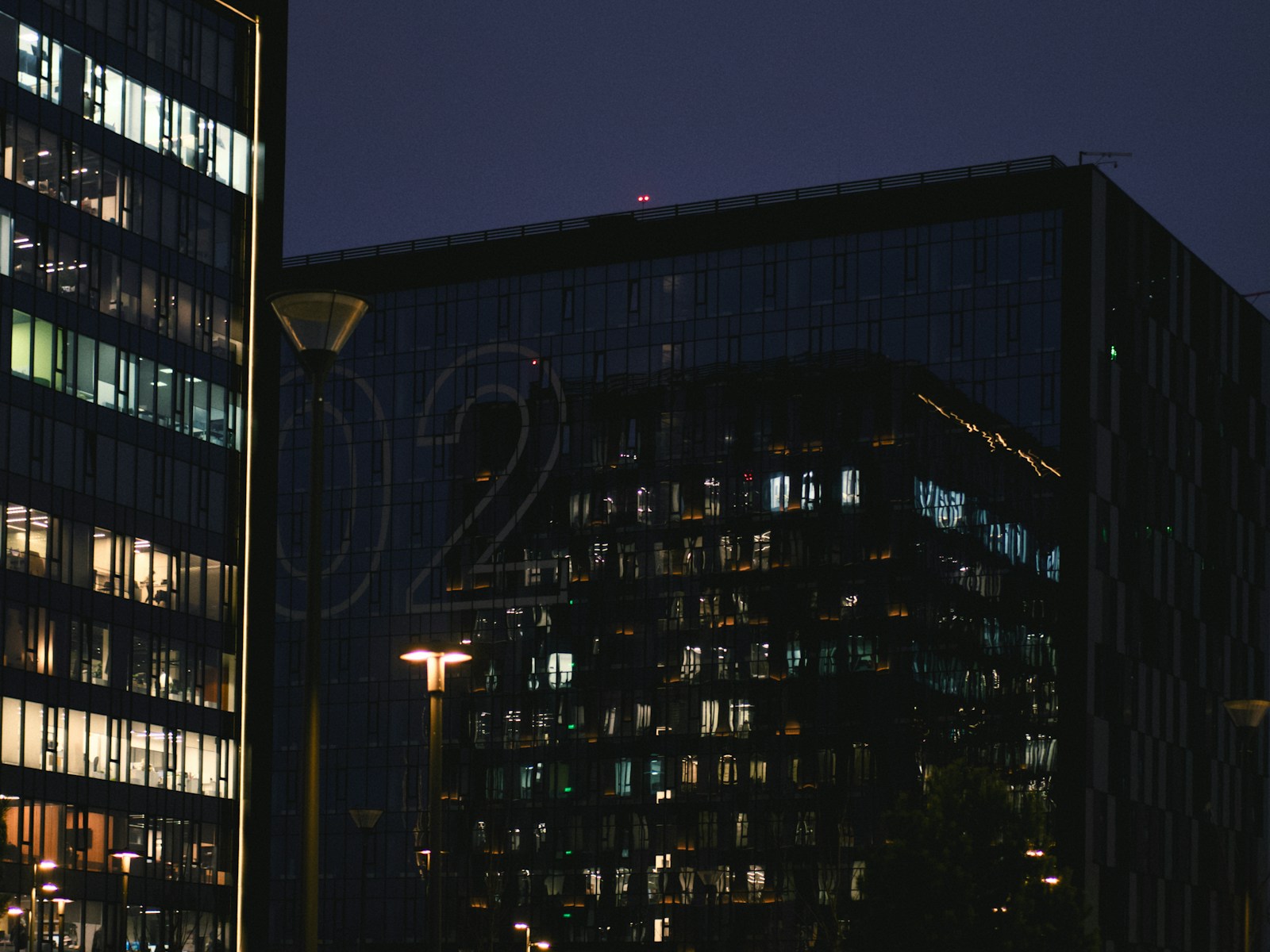 Office buildings after dark with scattered lit windows and glowing street lamps, long after most support teams log off
