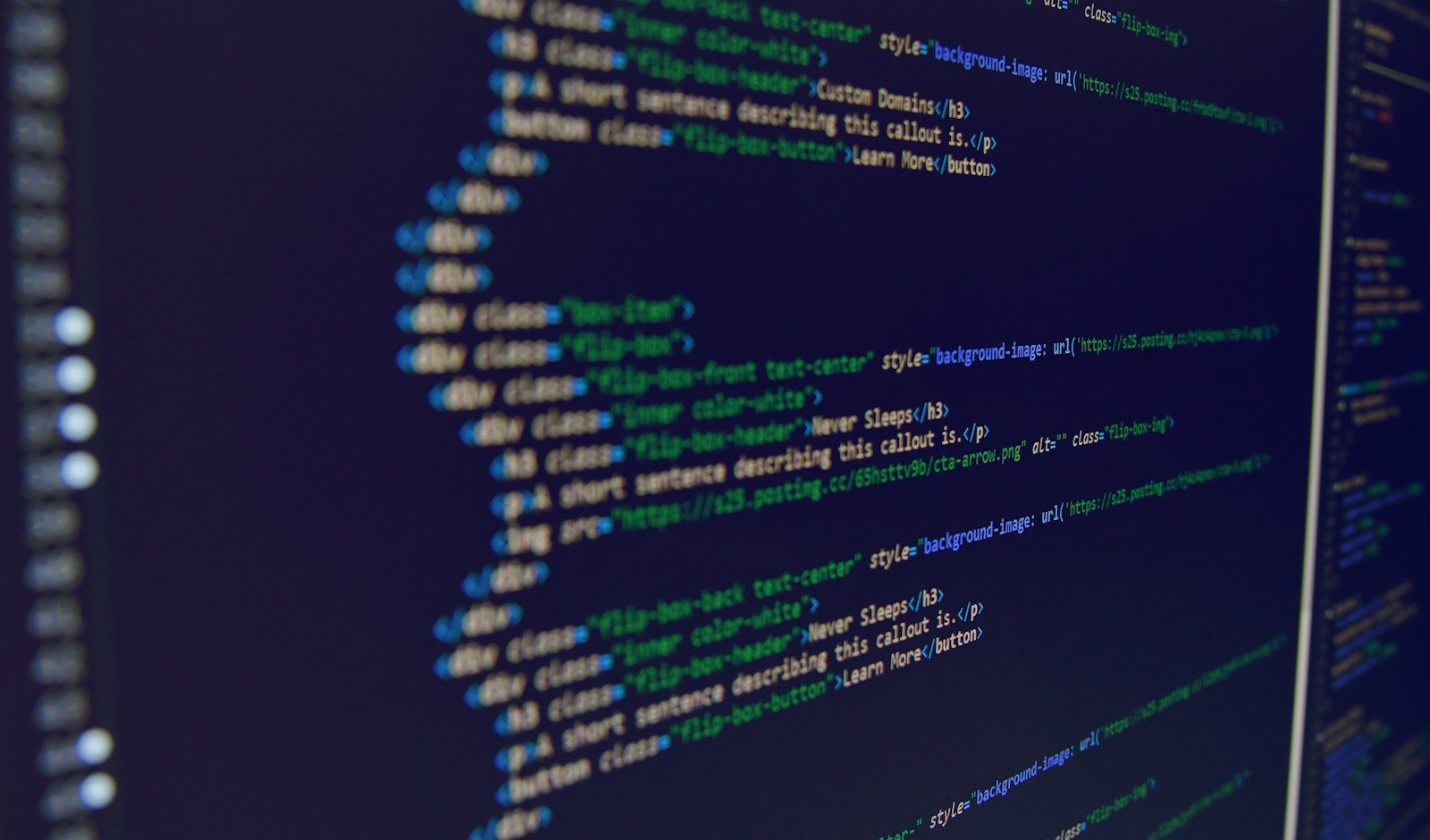 Close-up of a monitor showing HTML markup with div, h3 and button tags in a dark code editor