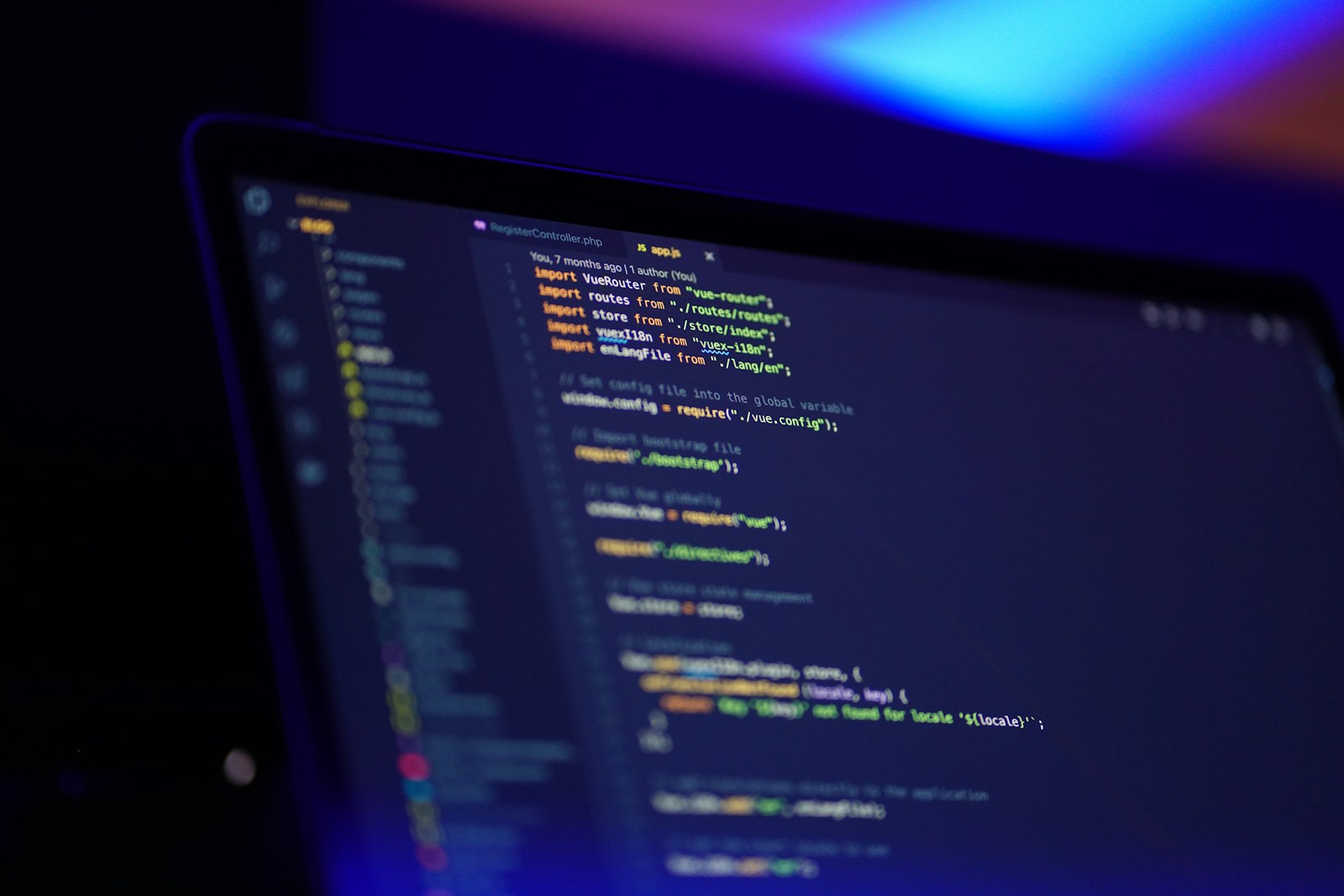 A laptop screen showing JavaScript code that imports Vue Router, lit by blue and purple light in a dark room