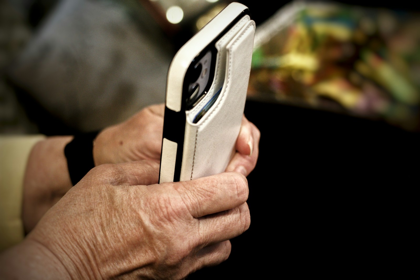Close-up of an older person's hands holding a smartphone in a white leather case
