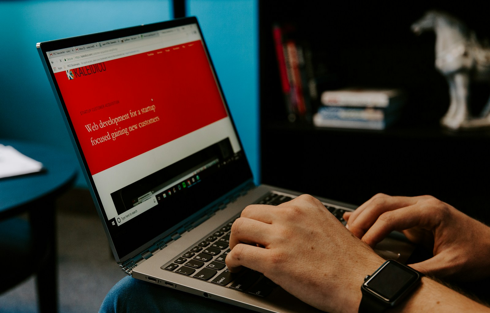 Hands type on a laptop showing a red web agency homepage about web development for startups