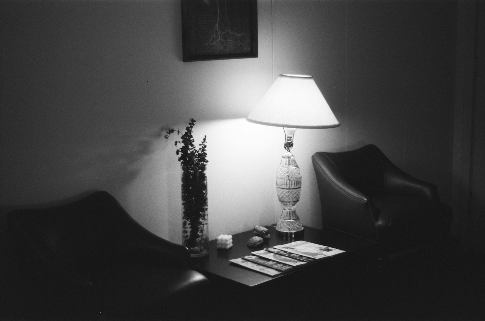 A dim waiting area with two leather armchairs, a lit table lamp and magazines on a side table