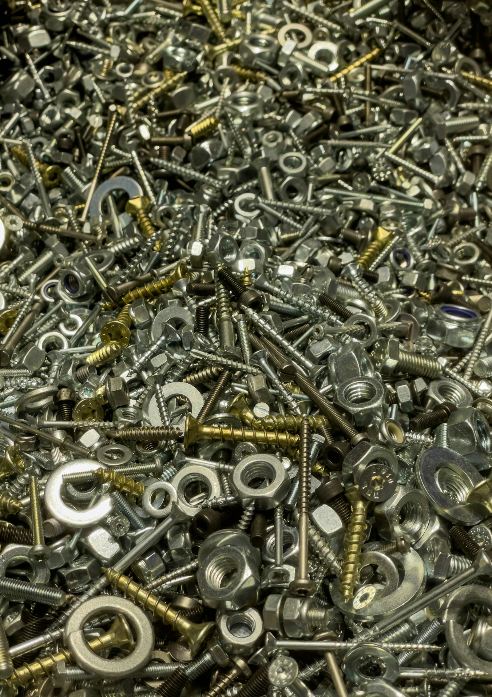 A dense pile of assorted zinc-plated and brass screws, hex nuts, bolts and washers