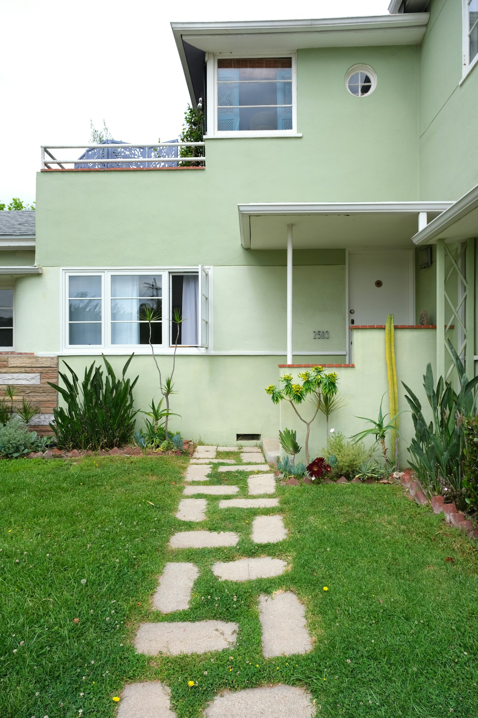 A pale green two-storey house with a stepping-stone path crossing a lawn to the front door, with succulents in the beds