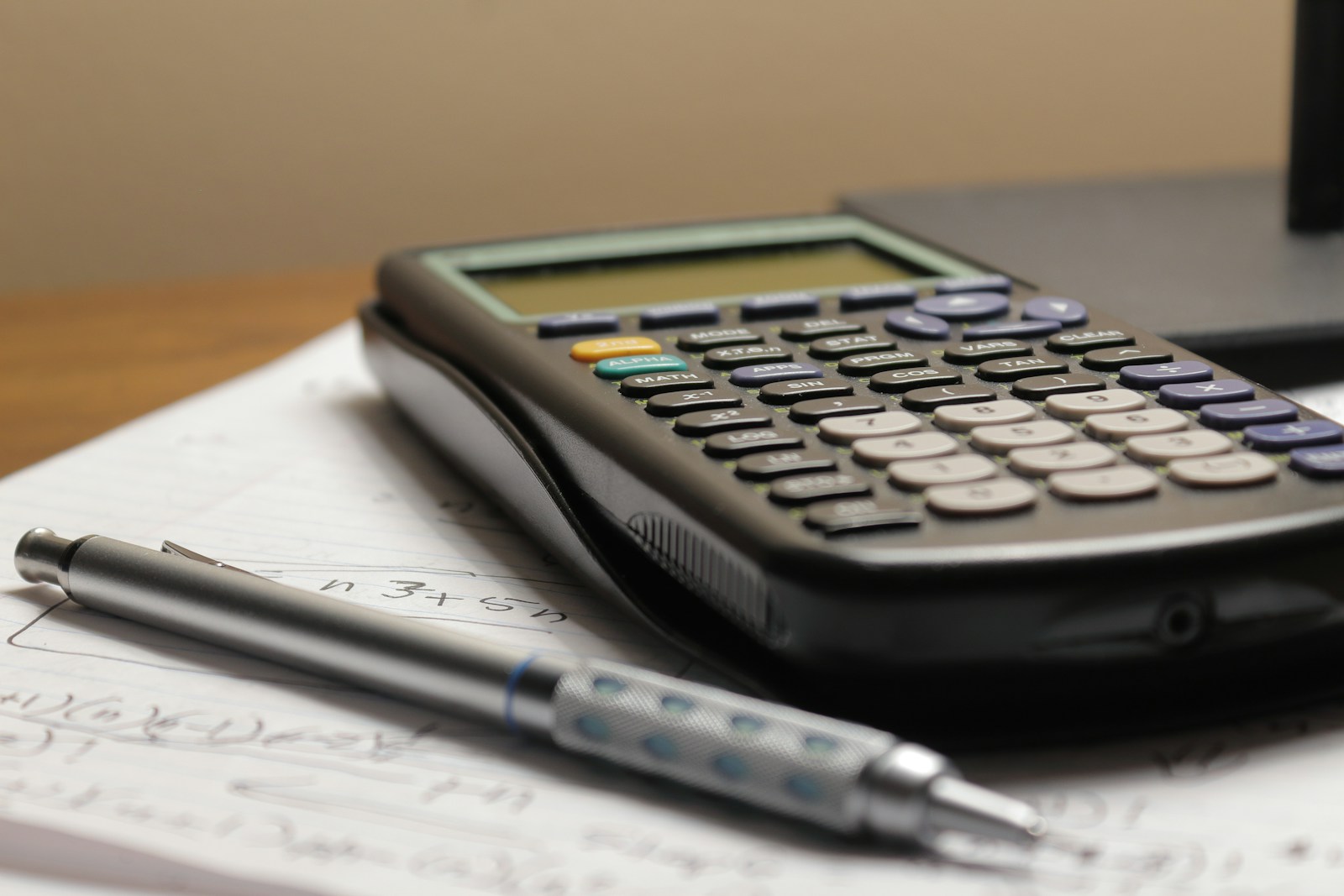 A graphing calculator and a mechanical pencil resting on a notepad covered in handwritten equations
