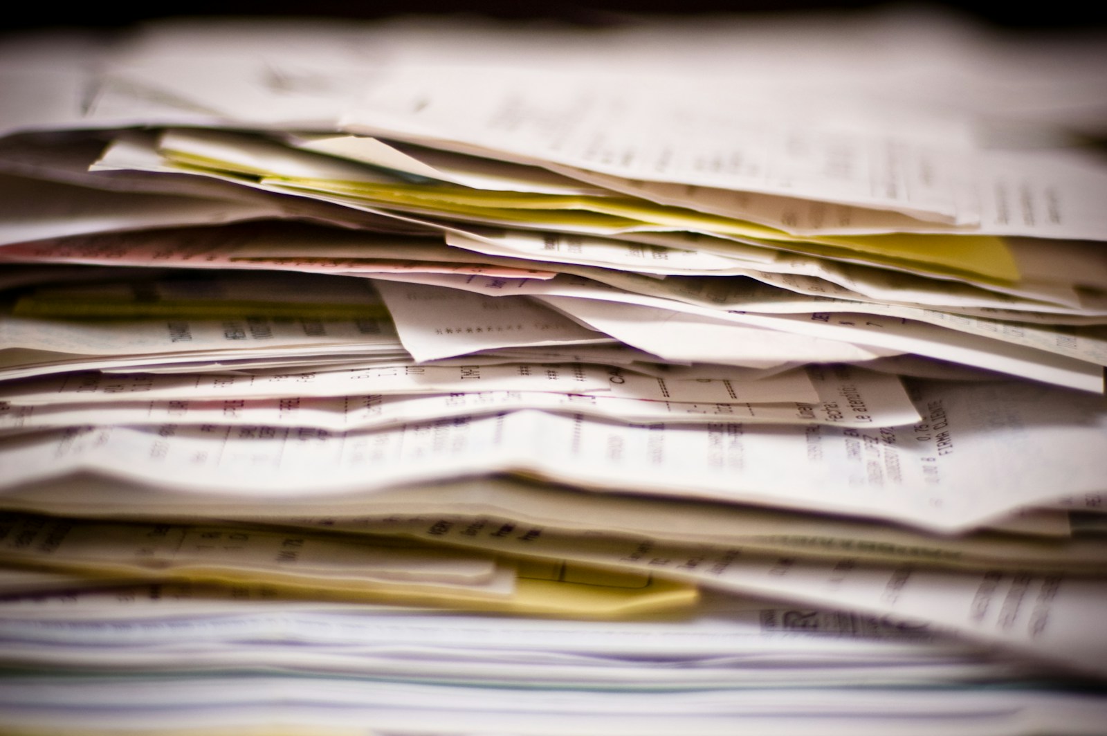 A close-up of a thick, uneven pile of folded receipts and printed invoices on a desk
