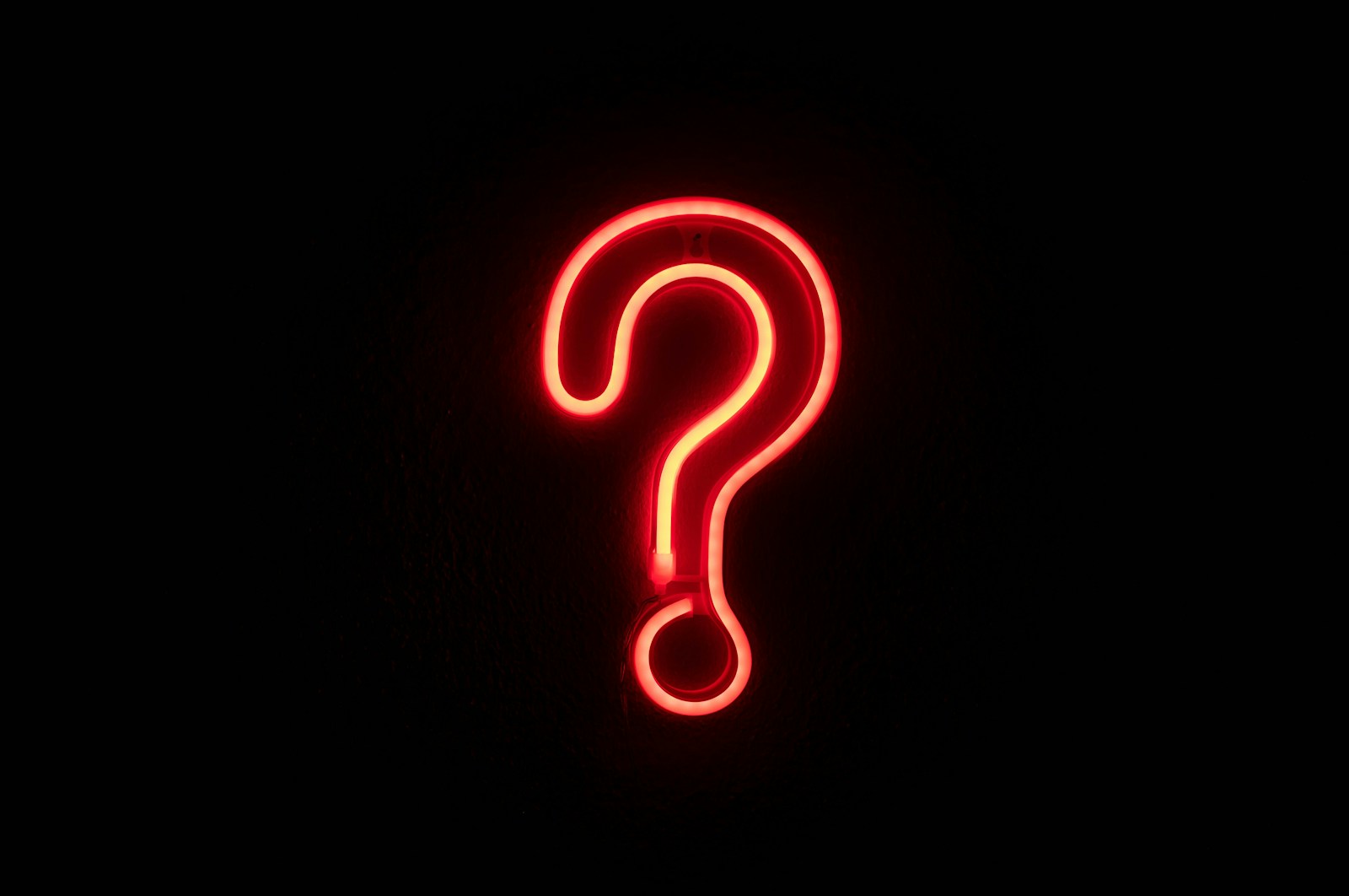 A glowing red neon question mark mounted on a dark wall, with nothing else in the frame