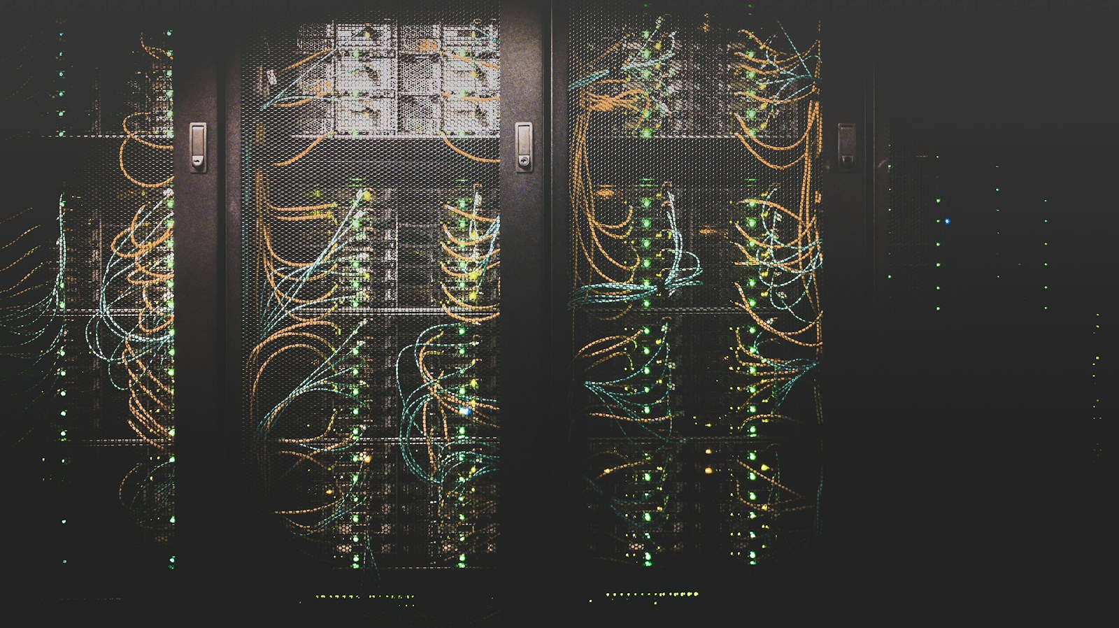 Open server racks in a dark room, filled with orange and teal network cables and rows of green status lights