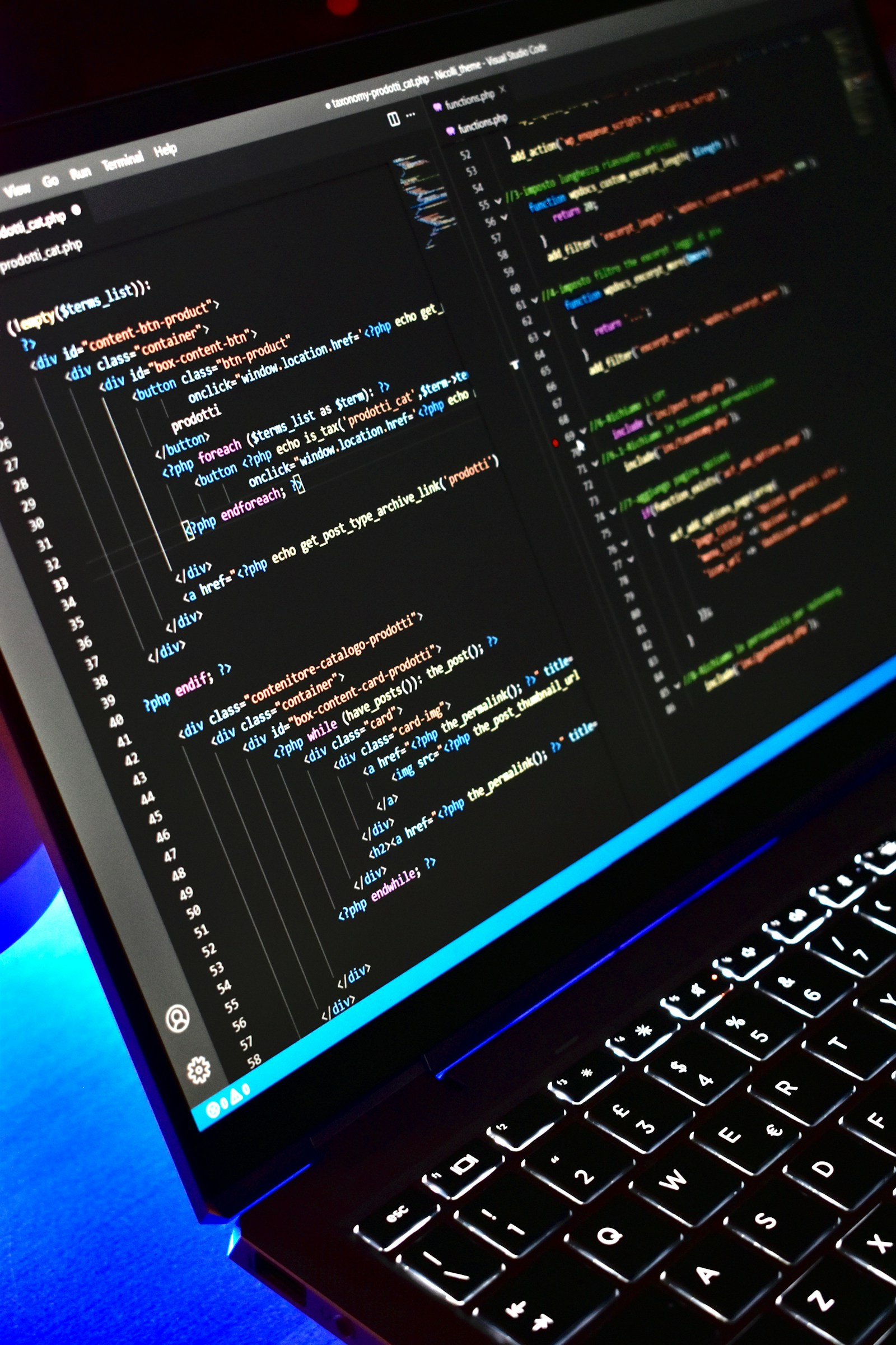 A laptop in blue light shows PHP and HTML template code in a code editor above backlit keys