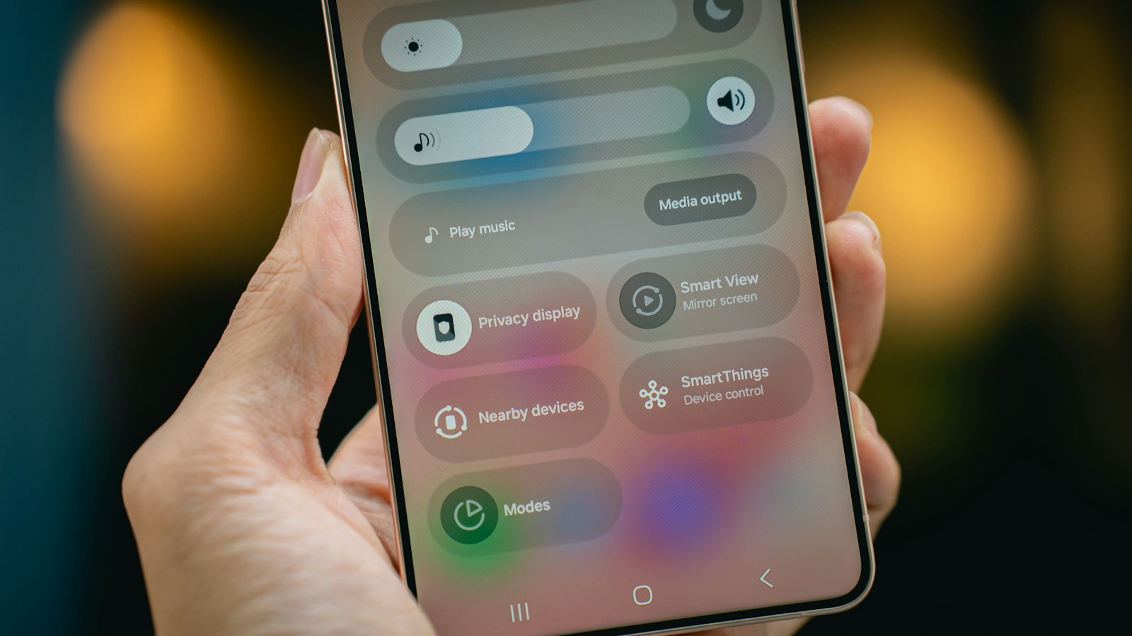 A hand holding a smartphone open on its quick settings panel, with a privacy display toggle among the tiles
