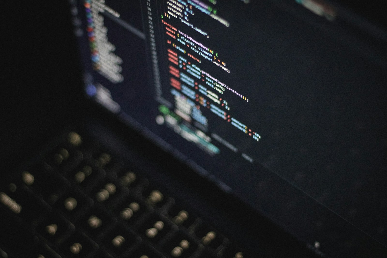 A dark laptop screen showing colorful JavaScript code, including a mouse-move handler, above a blurred keyboard