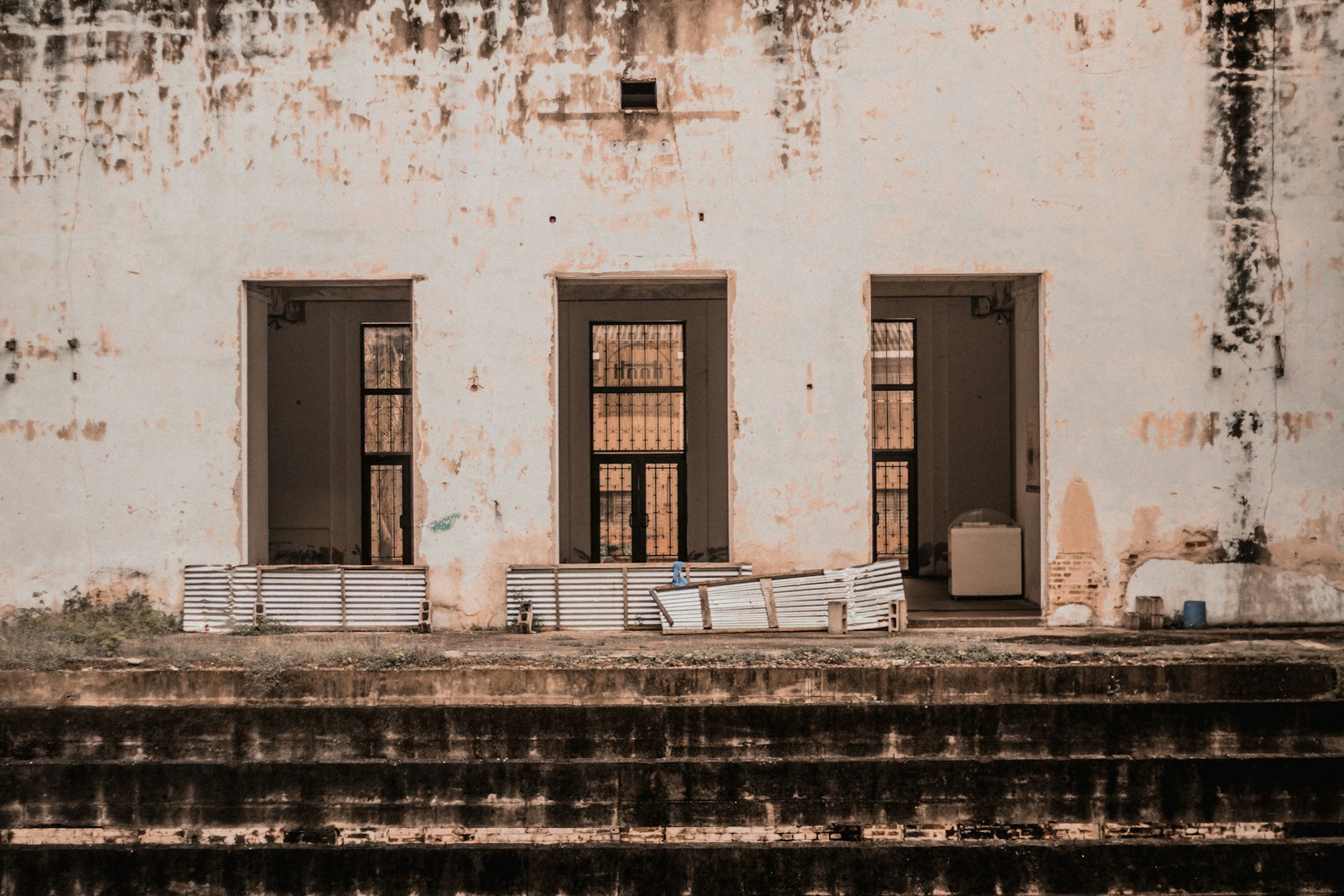 Three open doorways side by side in a weathered cream wall above a run of worn concrete steps