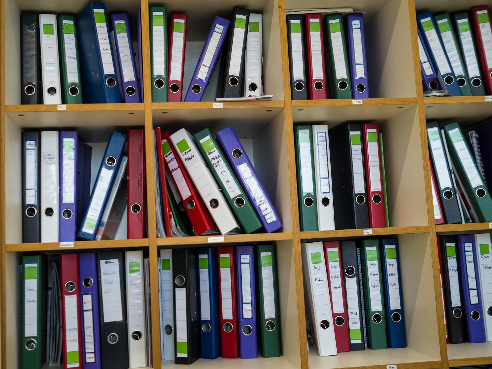 Wooden shelves packed with labelled ring binders in green, red, blue, purple, black and white