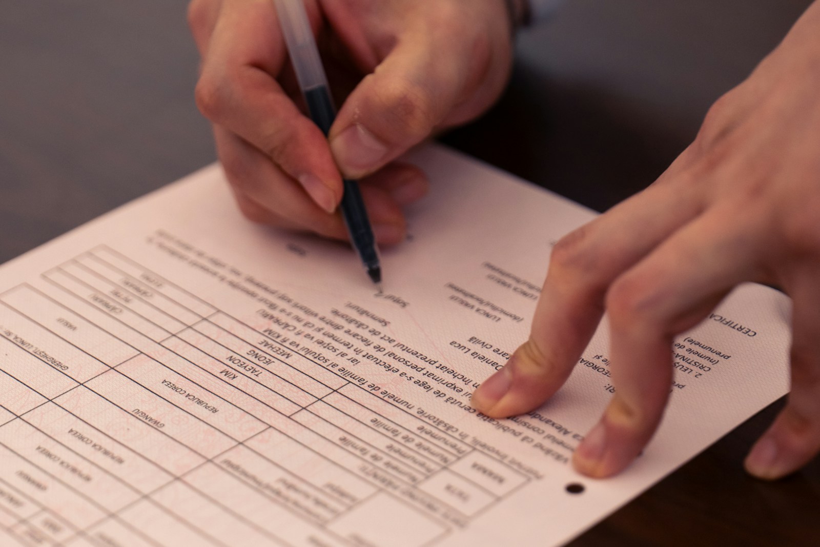 Close-up of a hand signing off a printed form with a ballpoint pen, the other hand holding the page flat