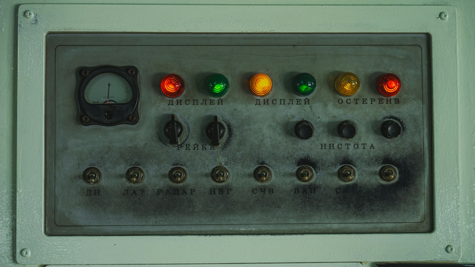 A grey control panel with a dial gauge, coloured indicator lights and a row of toggle switches, one per function