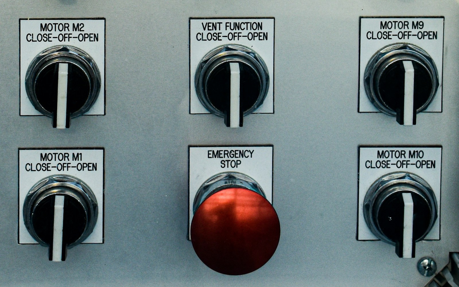 A metal control panel with labelled close-off-open rotary switches for motors and a vent beside a red emergency stop button