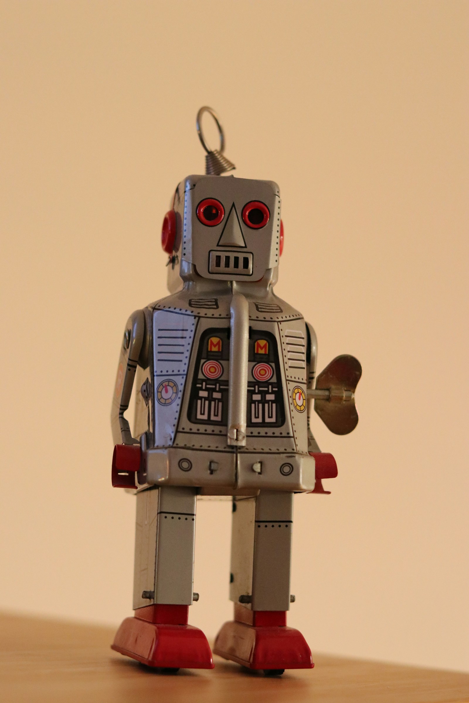 A vintage tin wind-up toy robot with red eyes and a brass key in its side stands on a wooden table