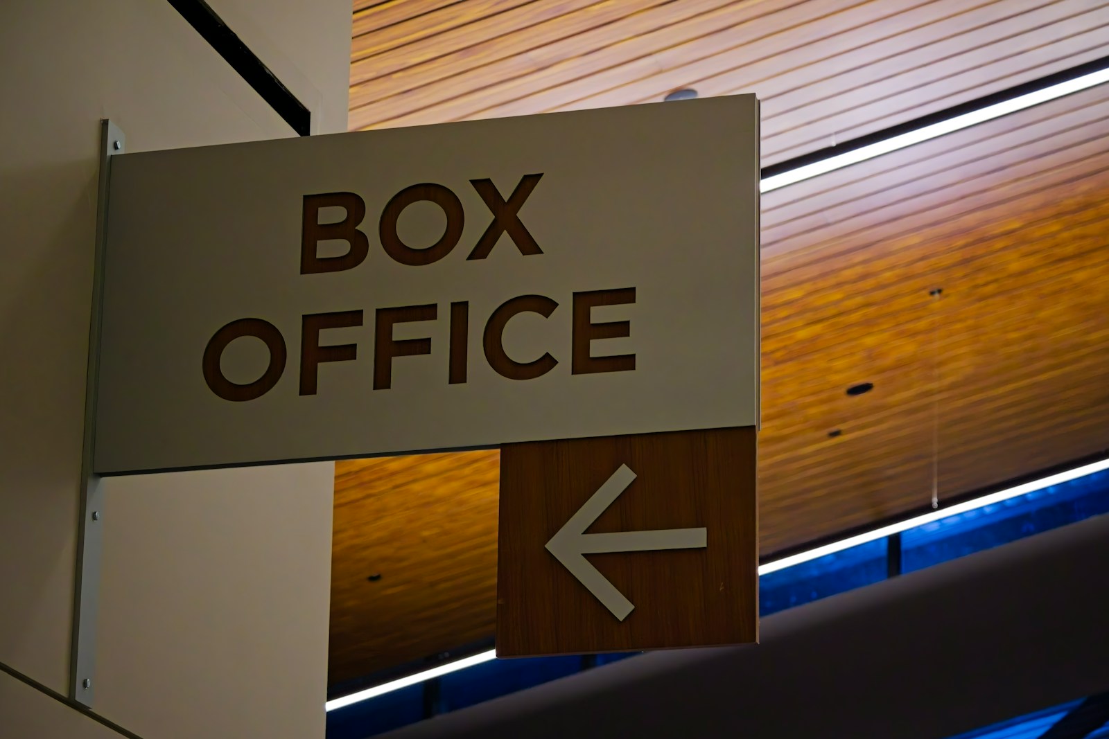 A wall-mounted sign reading BOX OFFICE with a left-pointing arrow beneath a slatted wooden ceiling