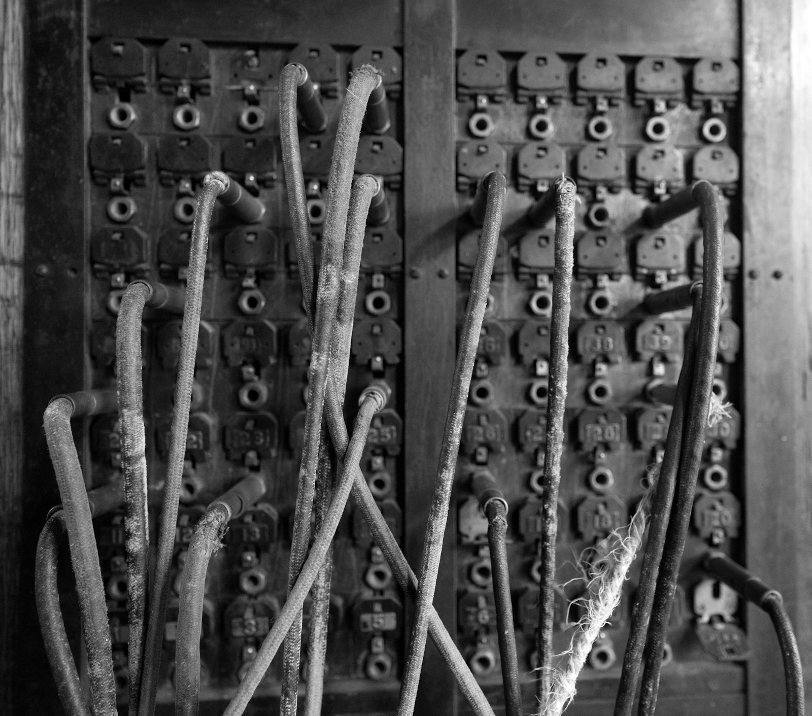 Close-up of an old telephone switchboard with dozens of numbered jacks and worn patch cords, in black and white