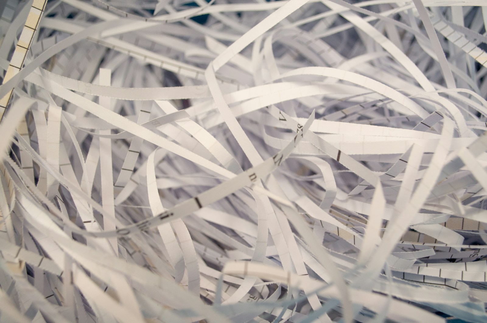 A close-up of a pile of white shredded paper strips, some printed with grid lines and stray letters