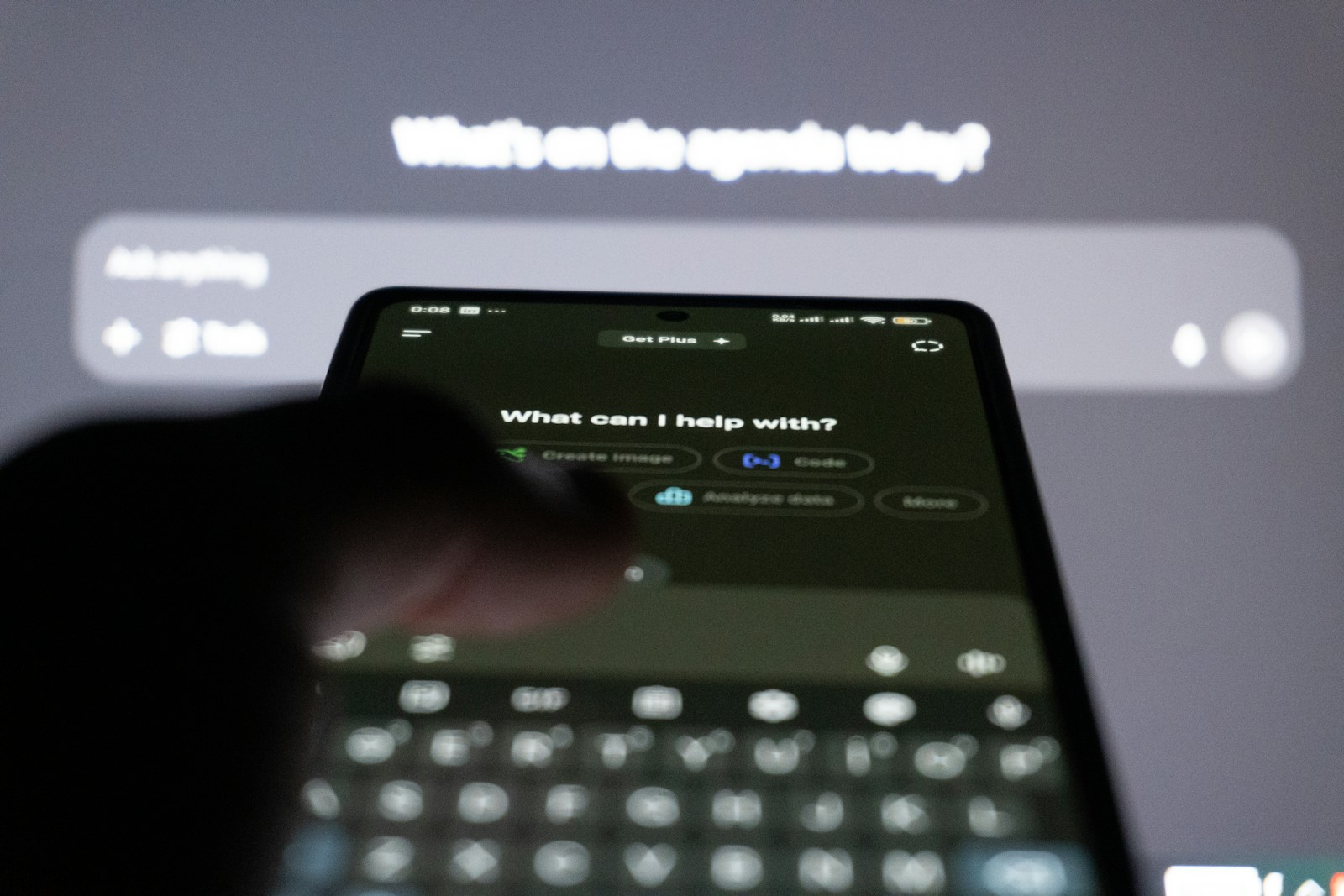 A finger hovers over a phone whose chat app asks What can I help with? above a row of suggestion buttons