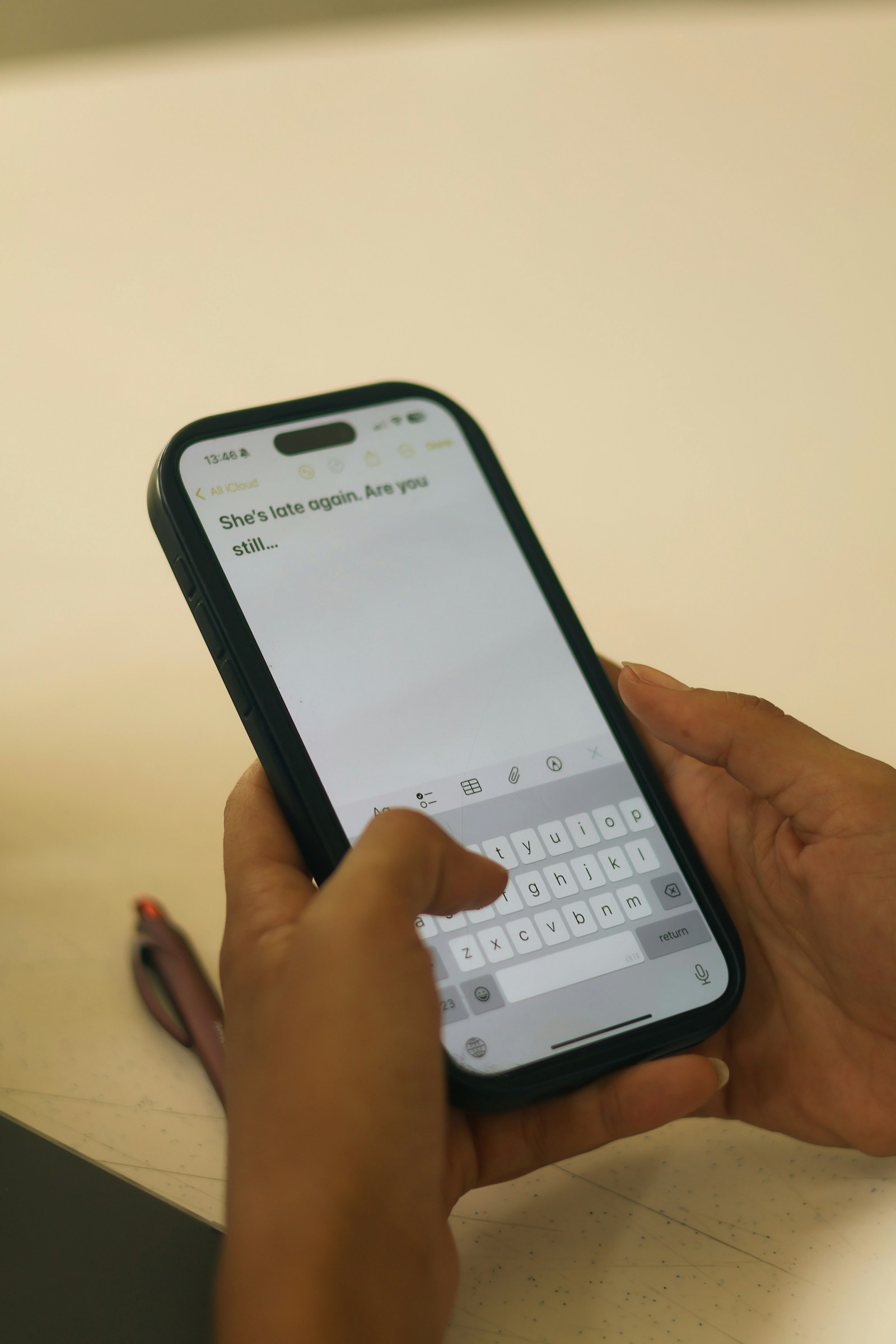 Two hands hold a smartphone while one thumb types a short message on the on-screen keyboard