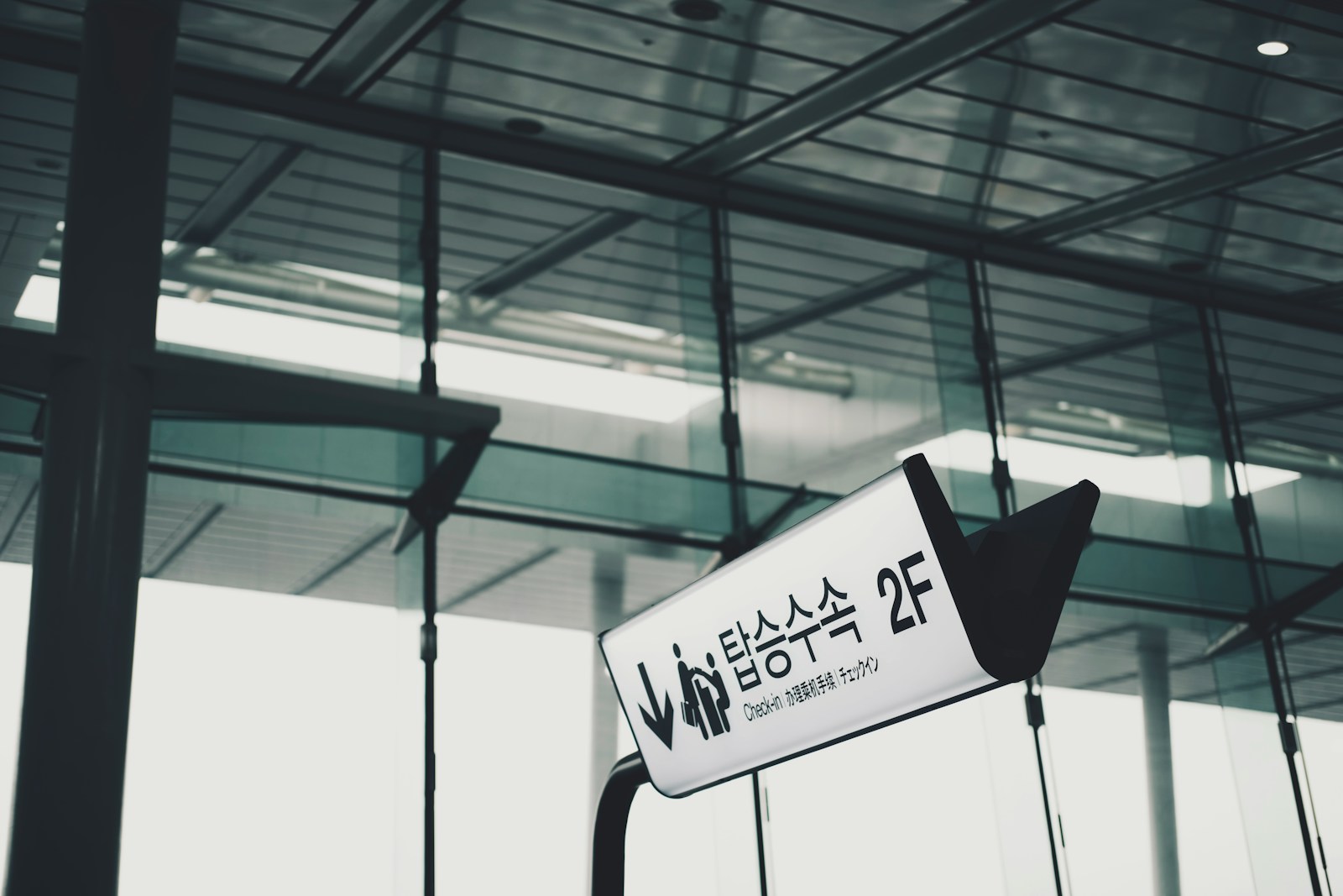 An illuminated airport sign with a downward arrow and a check-in icon points travellers to the second floor