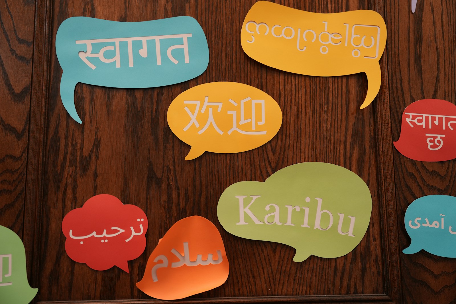 Colourful paper speech bubbles on a wooden wall say welcome in several languages, including Hindi, Chinese, Arabic and Swahili