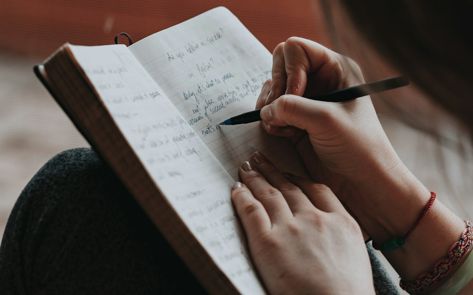 Over-the-shoulder view of a woman writing lines of handwritten text in an open notebook with a black pen