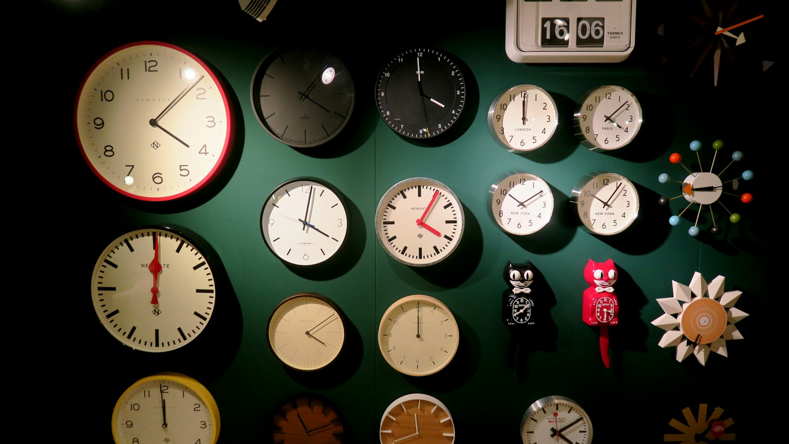 A dark green wall covered with dozens of different wall clocks, each showing a different time