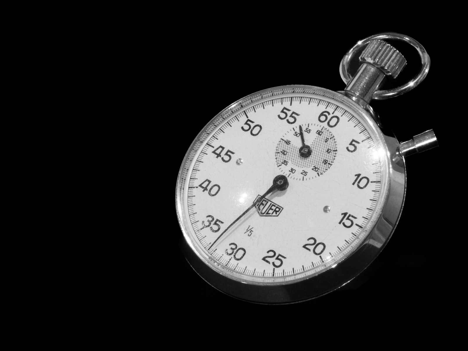 A vintage mechanical stopwatch with a white dial and silver case, lying on a glossy black surface