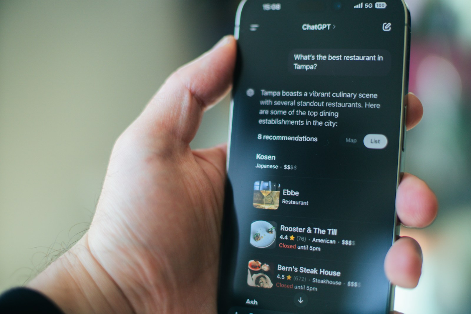A hand holds a phone where ChatGPT answers What's the best restaurant in Tampa with eight rated recommendations
