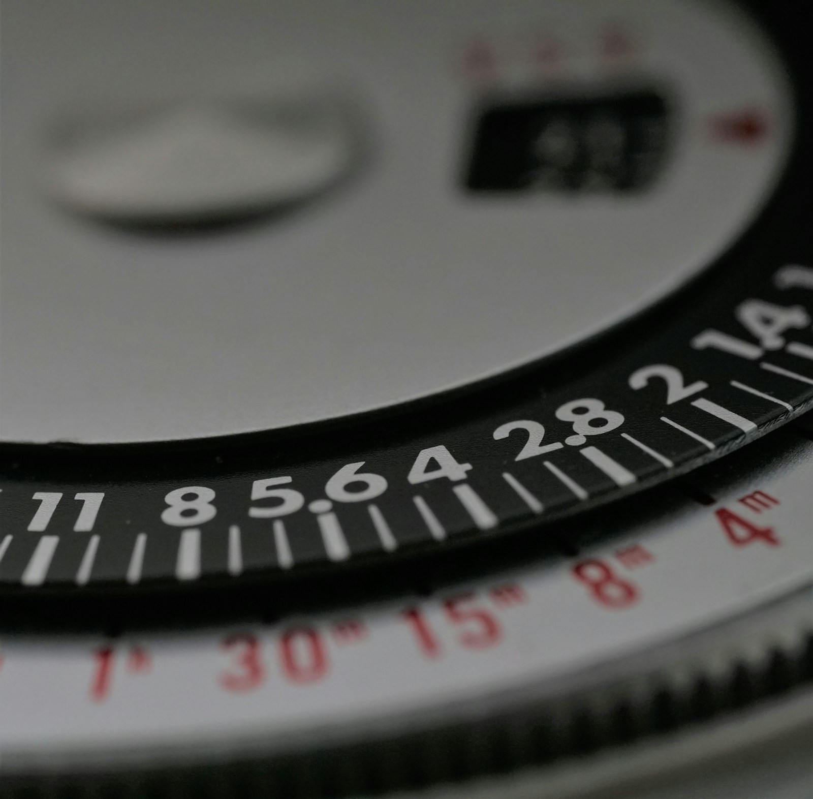 Close-up of an instrument dial with two scales, white f-numbers on a black ring and red time values on a silver ring