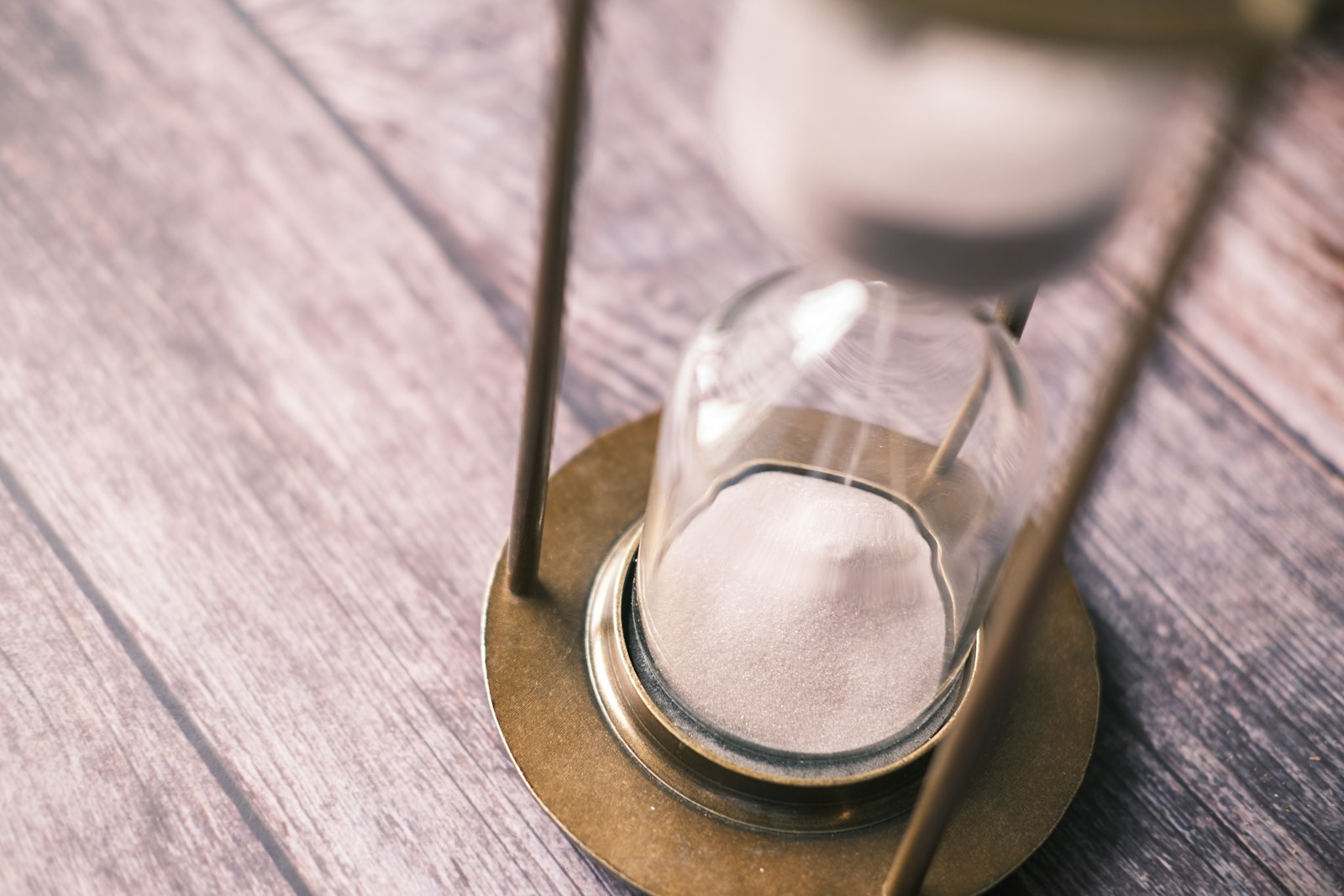 A brass hourglass stands on a weathered wooden table with its sand settled in the lower glass bulb