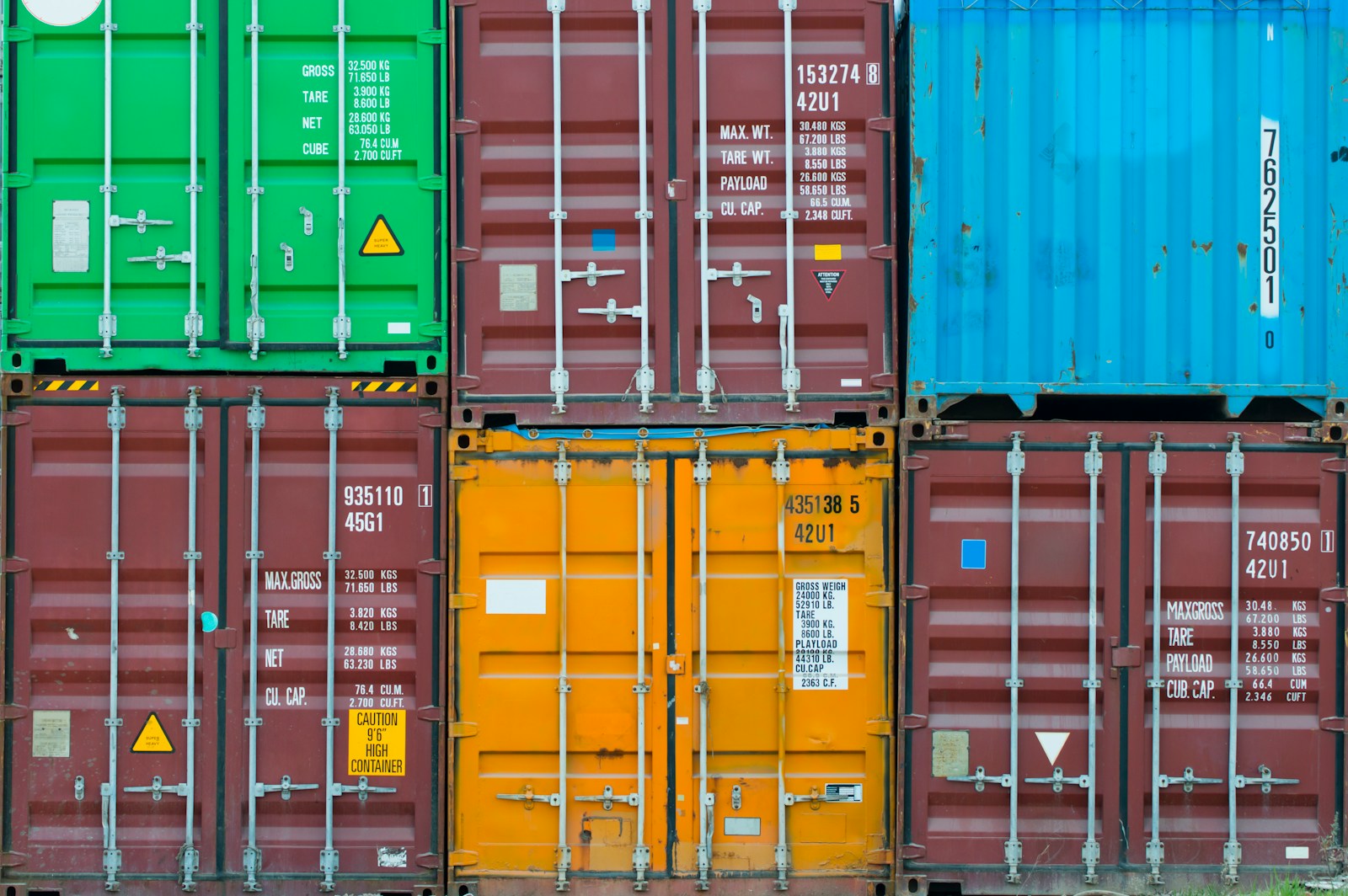 Six stacked shipping containers in green, maroon, blue and orange, their doors stencilled with weights and capacities