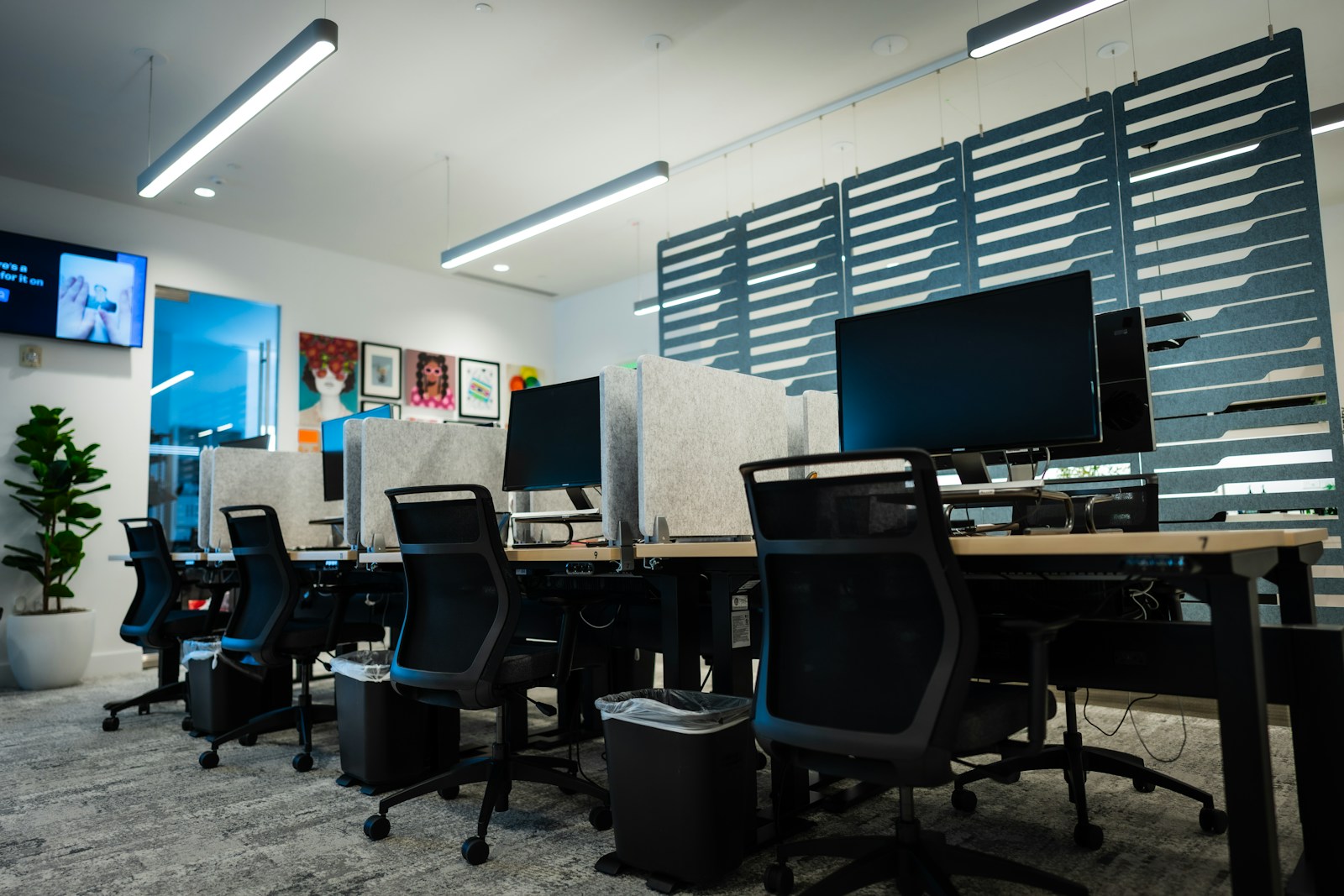 Rows of empty desks with dark monitors and black mesh chairs in a modern office with nobody at work