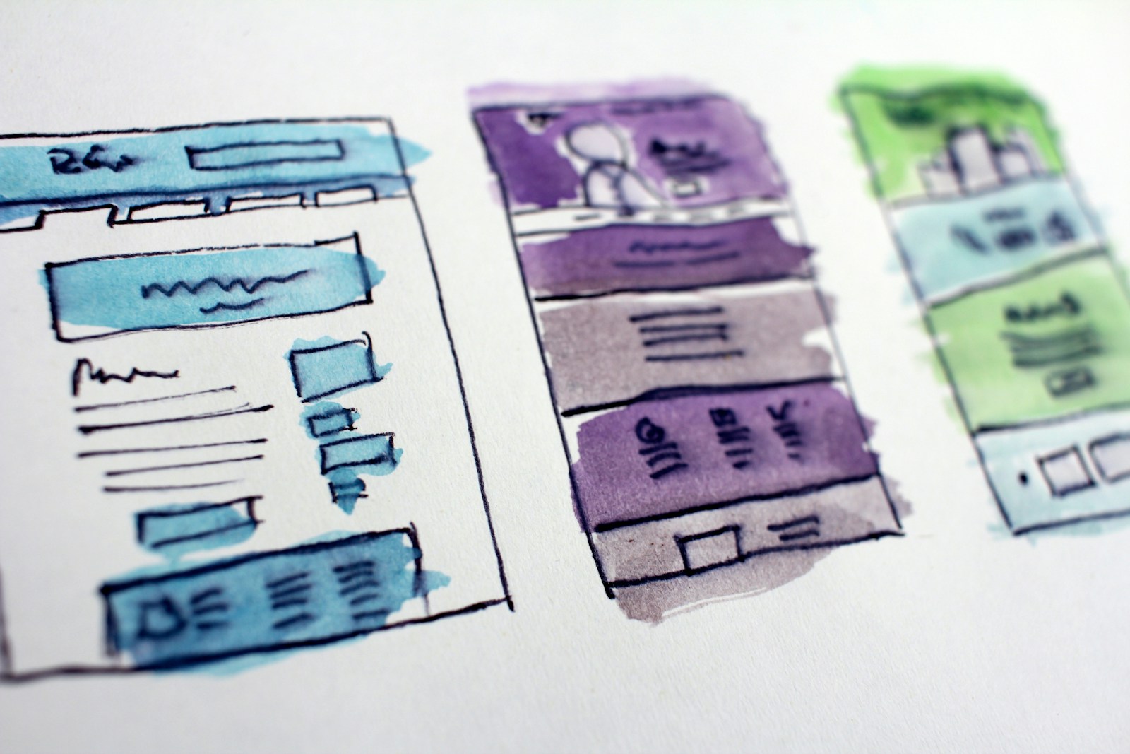 Watercolor sketches of three website page layouts in blue, purple and green, drawn as wireframes on white paper