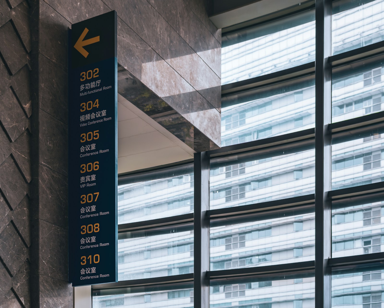 A tall wayfinding sign on a marble wall lists rooms 302 to 310, each with a short label, under an arrow