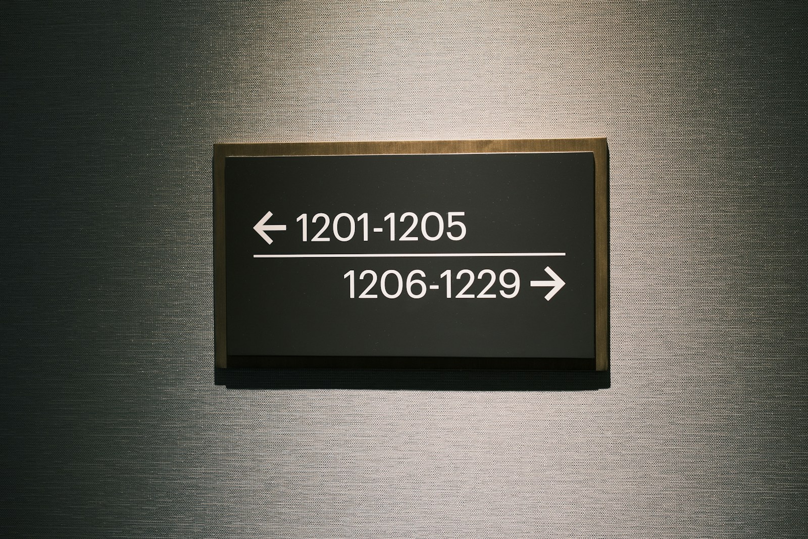 A dark wall sign with arrows points left to rooms 1201 to 1205 and right to rooms 1206 to 1229